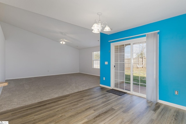 spare room with ceiling fan with notable chandelier, lofted ceiling, wood finished floors, and baseboards