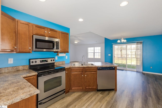 kitchen with light wood-style flooring, appliances with stainless steel finishes, a peninsula, brown cabinetry, and a sink