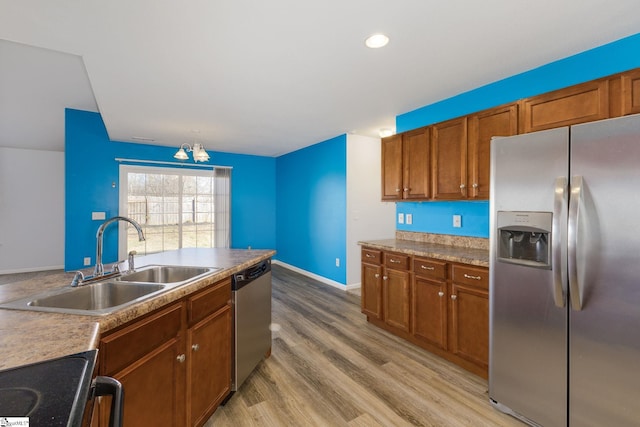 kitchen featuring baseboards, brown cabinets, light wood-style flooring, stainless steel appliances, and a sink