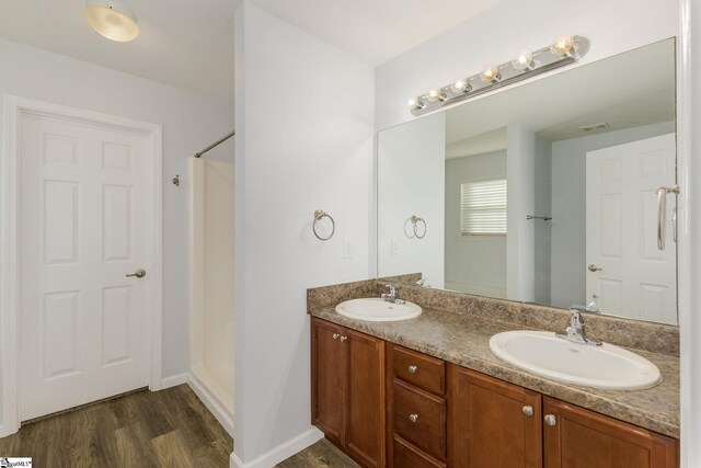 bathroom with a sink, a shower, wood finished floors, and double vanity