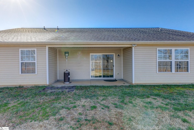 rear view of house with a patio, a yard, and roof with shingles