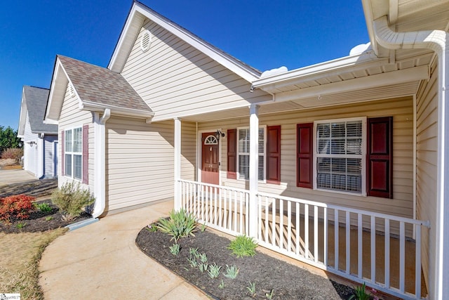 view of exterior entry featuring covered porch and a shingled roof