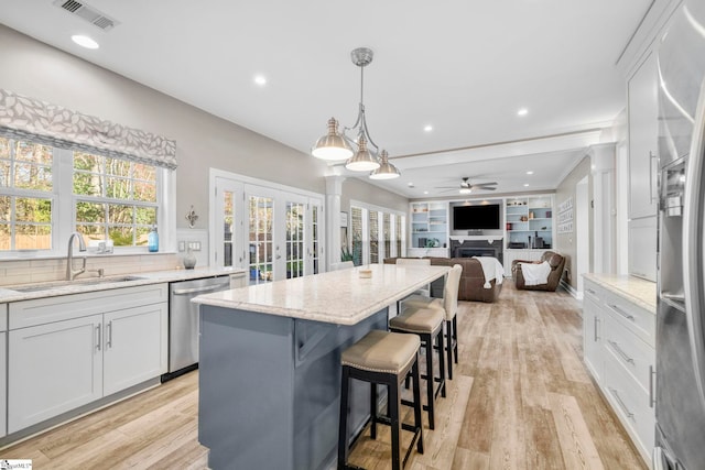 kitchen featuring visible vents, decorative columns, a fireplace, stainless steel appliances, and a sink