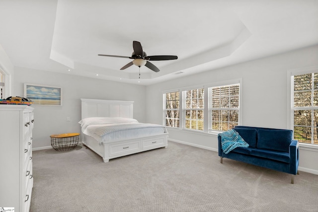 bedroom with a tray ceiling, light colored carpet, and baseboards