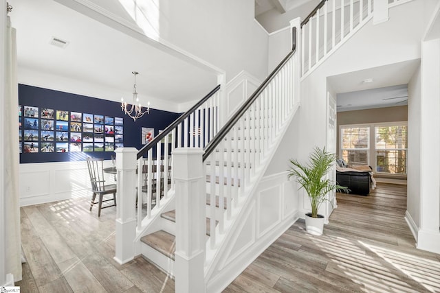 staircase featuring an inviting chandelier, a decorative wall, wood finished floors, and visible vents