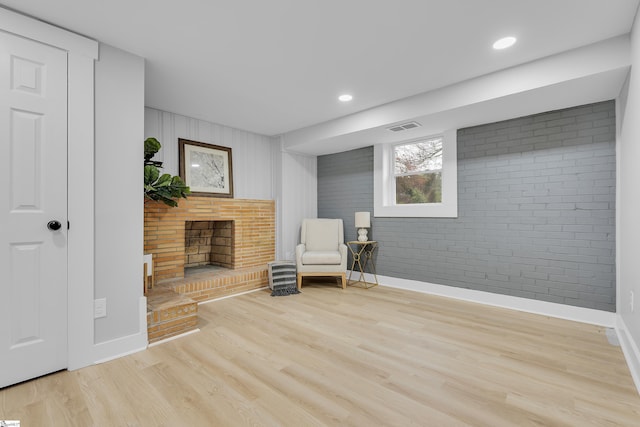 living area with visible vents, wood finished floors, brick wall, baseboards, and a brick fireplace