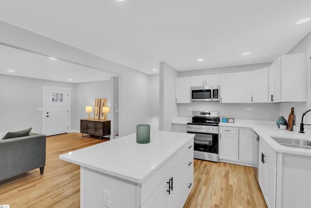 kitchen with light wood finished floors, a sink, stainless steel appliances, light countertops, and open floor plan