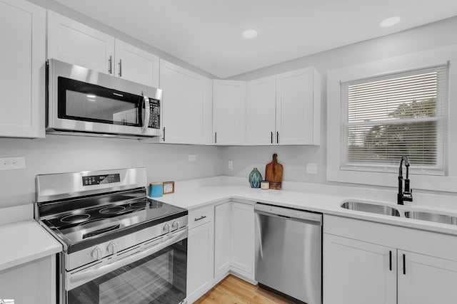 kitchen with white cabinets, stainless steel appliances, light countertops, and a sink