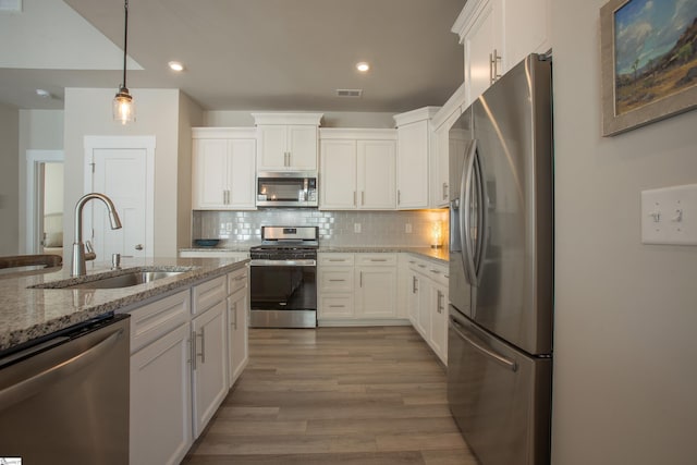 kitchen featuring a sink, wood finished floors, appliances with stainless steel finishes, white cabinets, and decorative backsplash