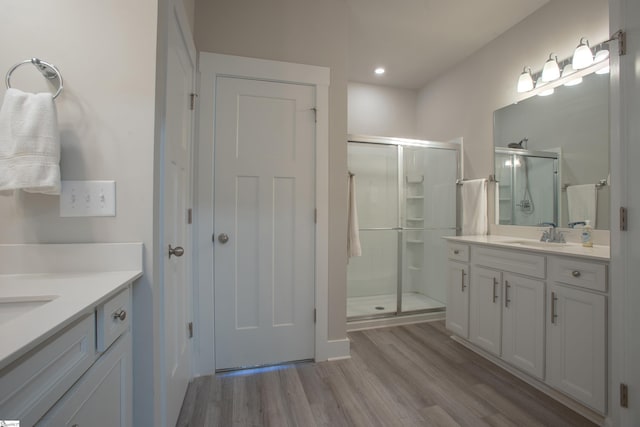 bathroom featuring a shower stall, two vanities, wood finished floors, and a sink