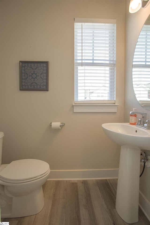 half bathroom with wood finished floors, toilet, and a healthy amount of sunlight