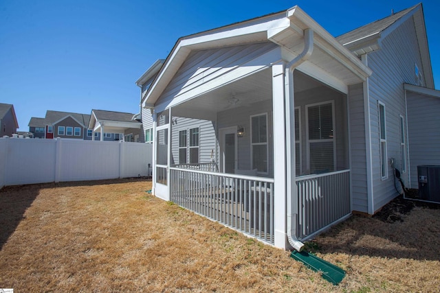 view of side of home with central air condition unit, a lawn, fence, and a sunroom