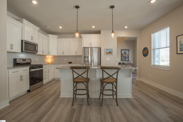 kitchen featuring tasteful backsplash, an island with sink, a kitchen bar, appliances with stainless steel finishes, and white cabinets