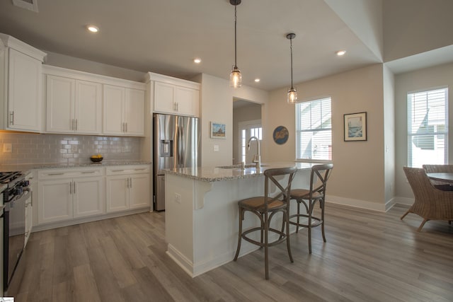 kitchen with stainless steel refrigerator with ice dispenser, a sink, backsplash, gas stove, and light wood-style floors