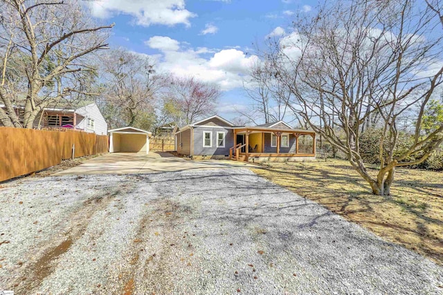 view of front facade with a porch, driveway, an outbuilding, and fence