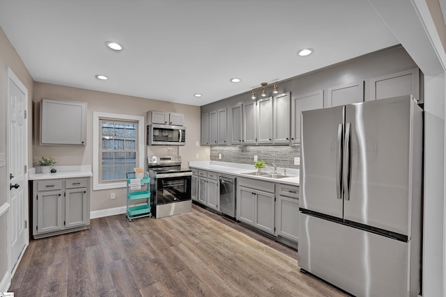 kitchen featuring tasteful backsplash, gray cabinets, appliances with stainless steel finishes, wood finished floors, and a sink