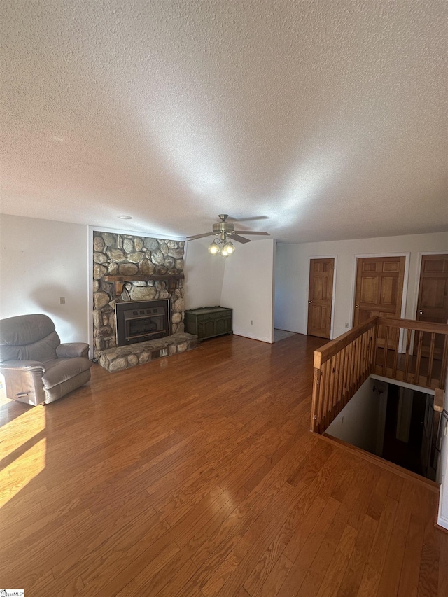 living room with ceiling fan, a textured ceiling, a stone fireplace, and wood finished floors