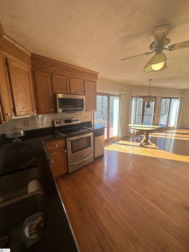 kitchen featuring brown cabinetry, a textured ceiling, stainless steel appliances, and dark wood-style flooring