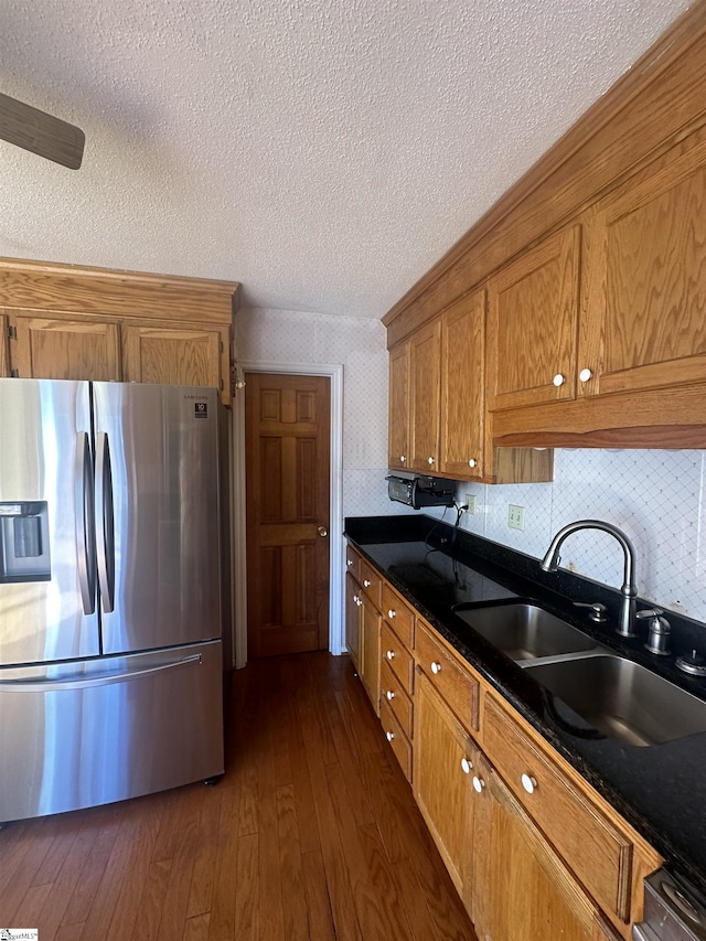 kitchen with dark wood-style floors, a sink, stainless steel refrigerator with ice dispenser, dark countertops, and brown cabinets