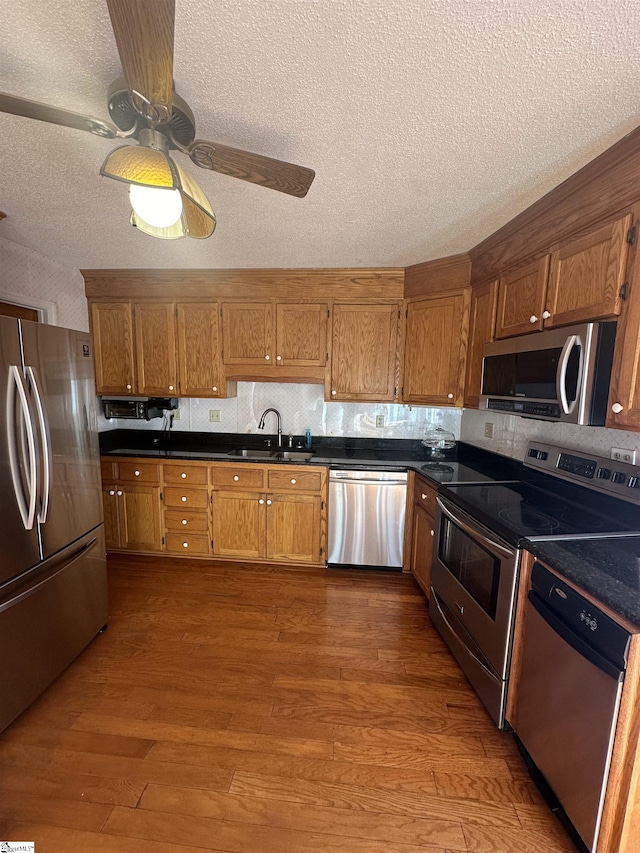 kitchen featuring wood finished floors, brown cabinets, stainless steel appliances, and a sink