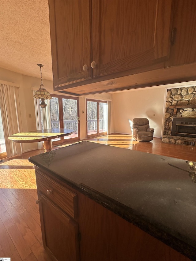 kitchen with decorative light fixtures, a textured ceiling, wood finished floors, a stone fireplace, and brown cabinetry