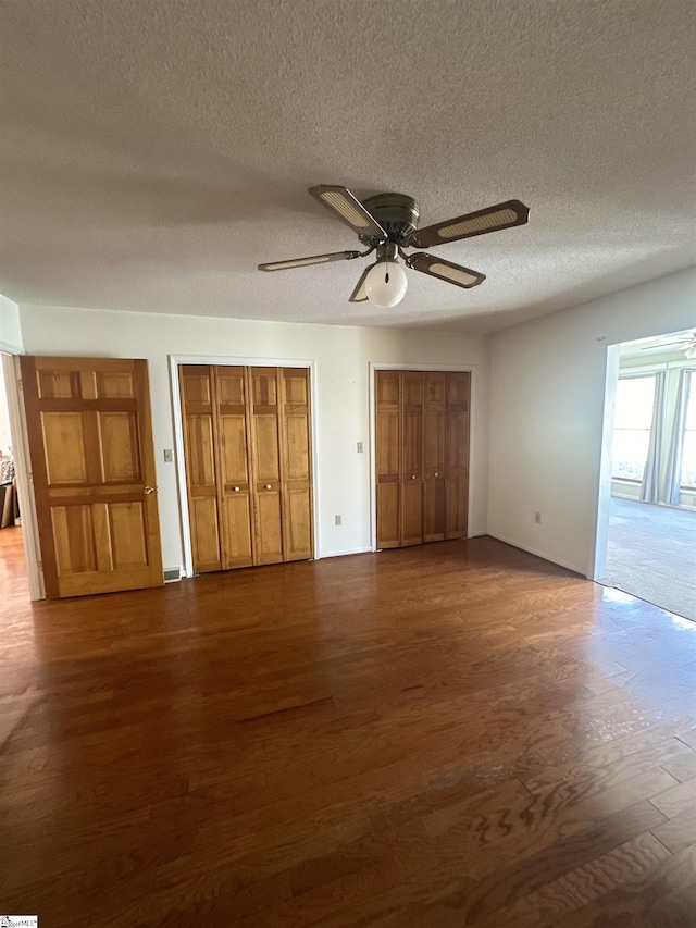 unfurnished bedroom with dark wood-style floors, a textured ceiling, two closets, and ceiling fan