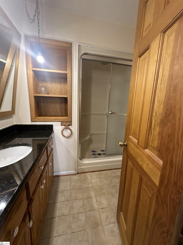 bathroom with baseboards, vanity, a shower stall, and a textured ceiling