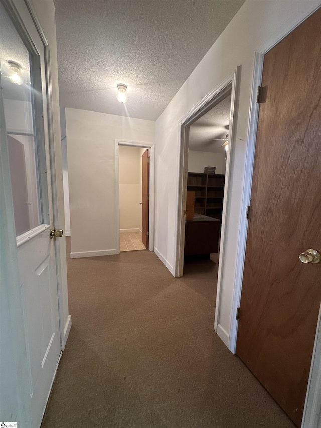 hallway featuring carpet flooring, a textured ceiling, and baseboards