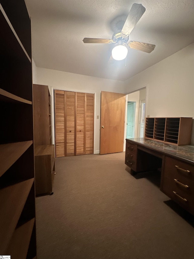 unfurnished bedroom with built in study area, ceiling fan, carpet floors, a closet, and a textured ceiling