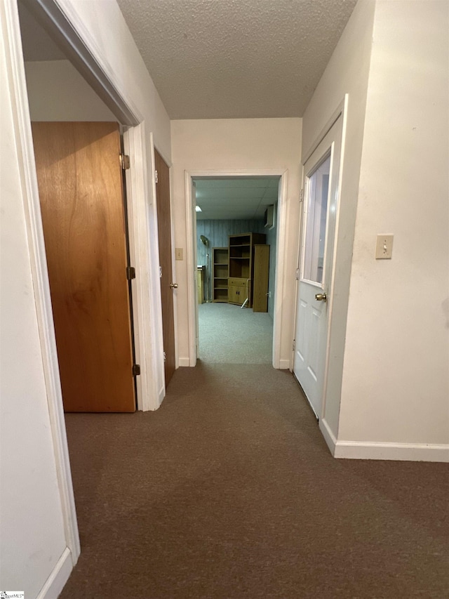 corridor featuring baseboards, carpet floors, and a textured ceiling