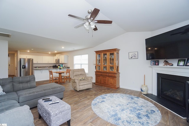 living area featuring visible vents, a fireplace with raised hearth, baseboards, lofted ceiling, and light wood-style flooring