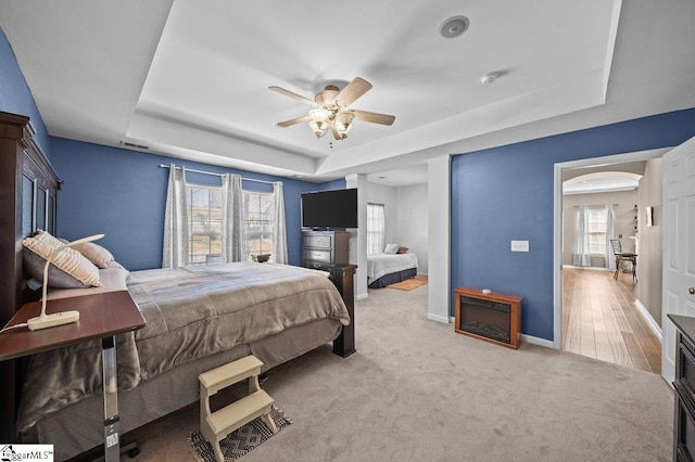 carpeted bedroom featuring a tray ceiling, baseboards, visible vents, and ceiling fan