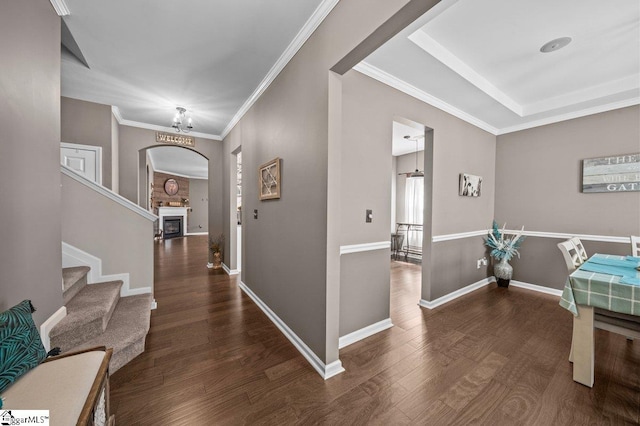 foyer entrance with ornamental molding, wood finished floors, arched walkways, a fireplace, and baseboards