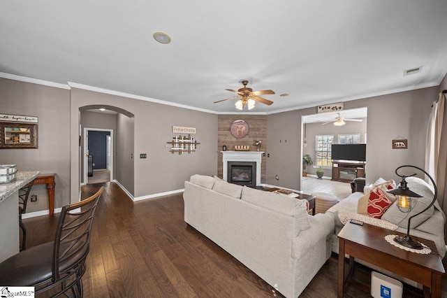 living room featuring crown molding, baseboards, dark wood-style floors, arched walkways, and a glass covered fireplace