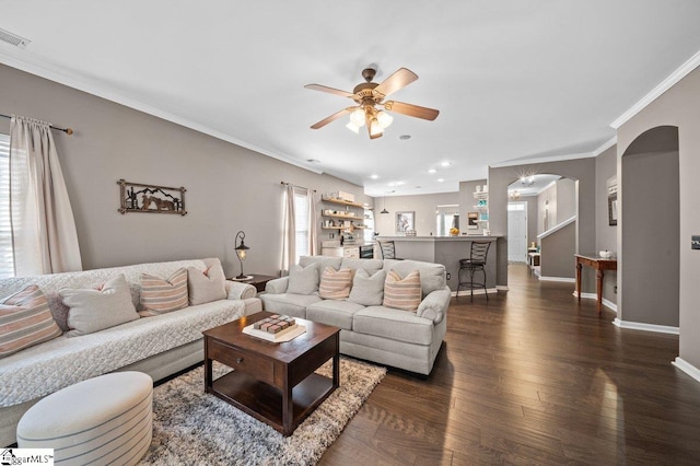 living room with crown molding, baseboards, dark wood-style floors, arched walkways, and a ceiling fan