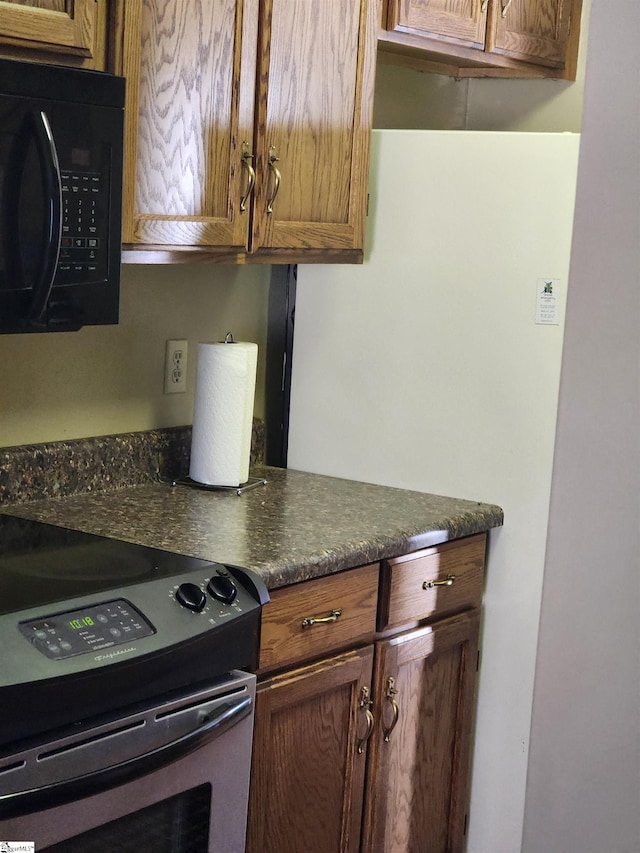 kitchen featuring electric range, brown cabinets, dark countertops, and black microwave