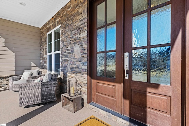 view of exterior entry with french doors, stone siding, and covered porch