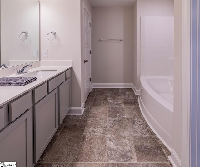 bathroom with vanity, a bathing tub, baseboards, and stone finish flooring