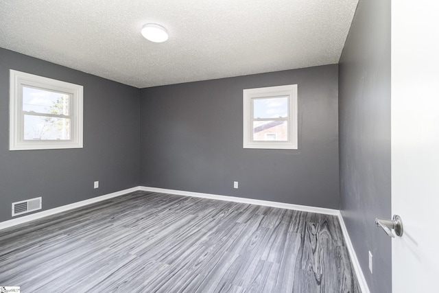 spare room with visible vents, baseboards, a textured ceiling, and wood finished floors