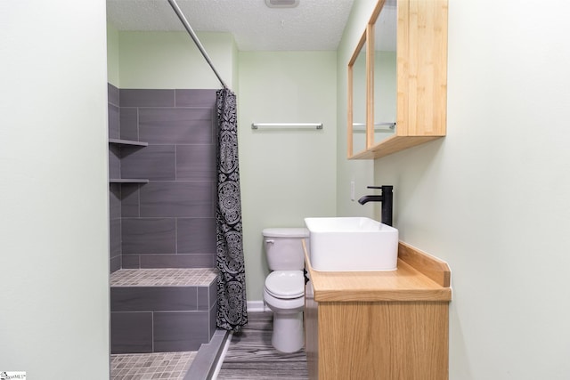 bathroom featuring toilet, a textured ceiling, wood finished floors, tiled shower, and vanity