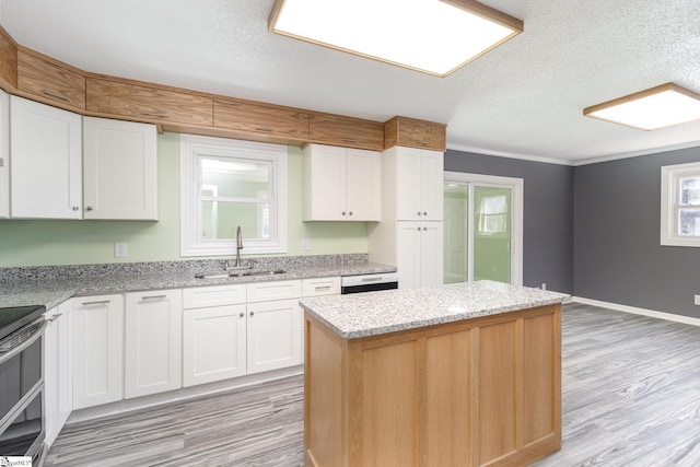 kitchen featuring light wood finished floors, a kitchen island, range with two ovens, white cabinets, and a sink