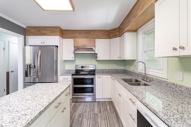 kitchen with a sink, wood finished floors, range hood, appliances with stainless steel finishes, and white cabinets