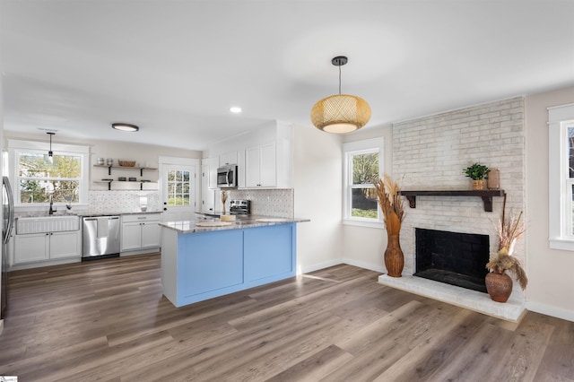 kitchen with a brick fireplace, backsplash, appliances with stainless steel finishes, and white cabinets