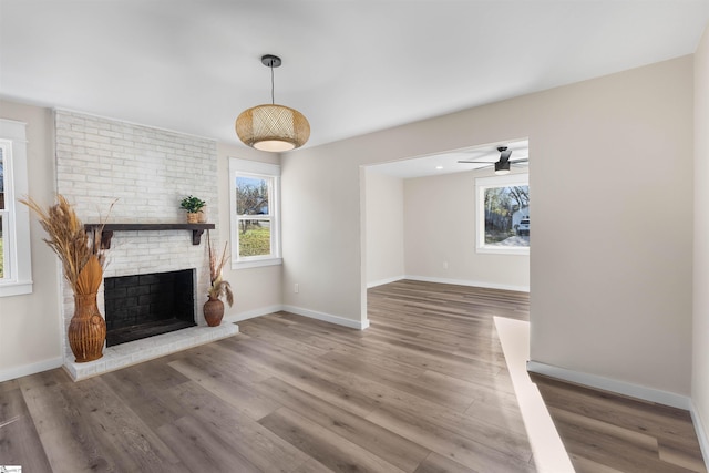 unfurnished living room featuring a ceiling fan, wood finished floors, a fireplace, and baseboards