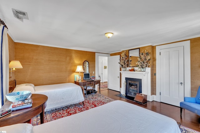 bedroom with visible vents, a fireplace with raised hearth, wood finished floors, and ornamental molding