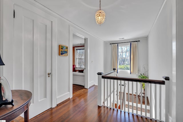 hallway with visible vents, baseboards, dark wood finished floors, crown molding, and an upstairs landing