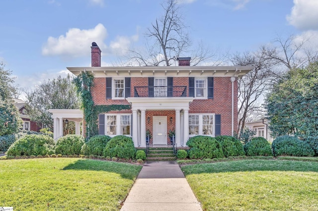 view of front of home featuring brick siding, a chimney, a front lawn, and a balcony