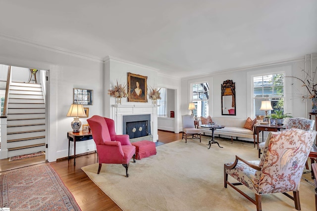 living room with stairway, wood finished floors, baseboards, a fireplace with flush hearth, and ornamental molding