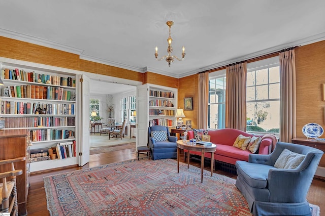 living area with built in shelves, an inviting chandelier, wood finished floors, and ornamental molding