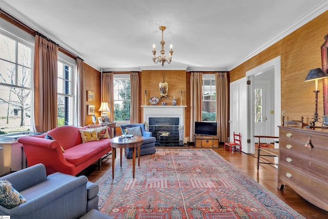 living area with an inviting chandelier, crown molding, a fireplace with flush hearth, and wood finished floors